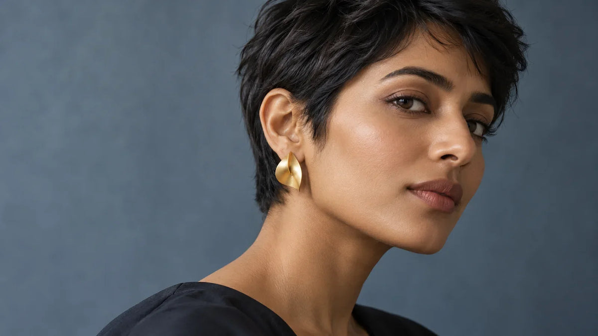 Conceptual editorial close-up of a South Asian model with a short textured crop, one ear visible and a sculptural earring; AI-generated, not an ARVENIER product photo.