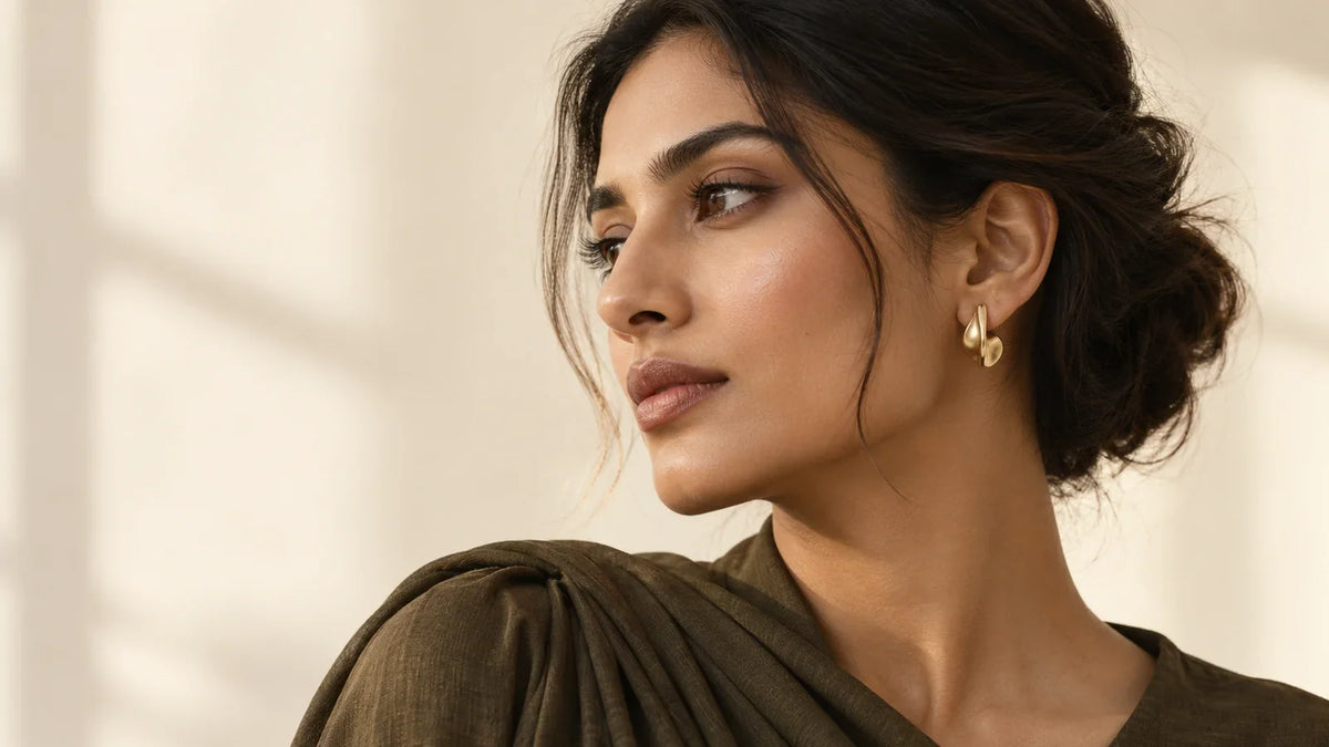 Conceptual editorial portrait of a South Asian model wearing a small sculptural earring; AI-generated, not an ARVENIER product photograph.