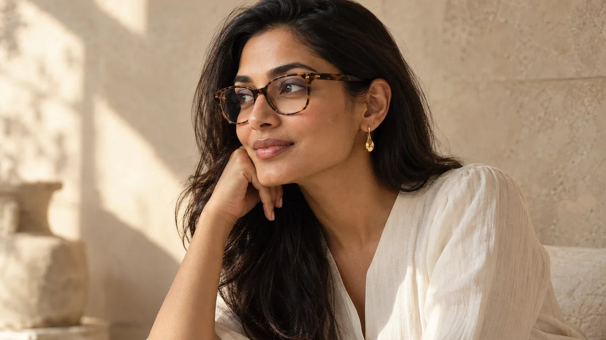 Indian woman in tortoiseshell glasses and a gold drop earring, with her hair tucked behind one ear.