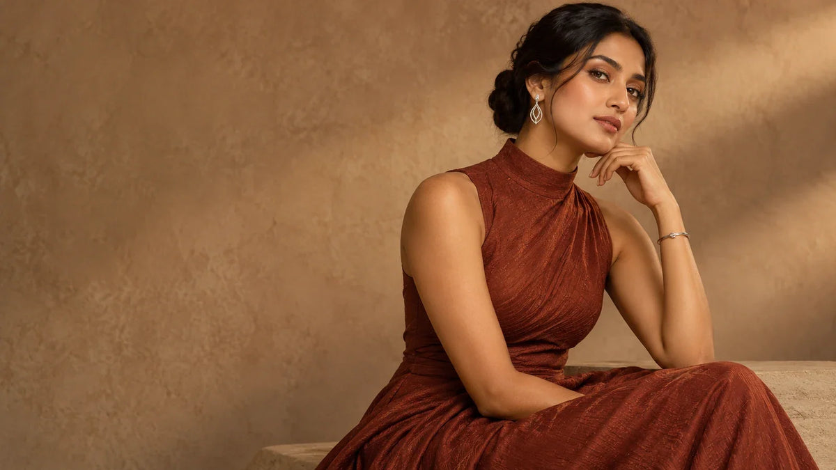 Conceptual editorial of a South Asian model in a terracotta high-neck dress with sculptural earrings and a slim bracelet; AI-generated, not an ARVENIER product photo.
