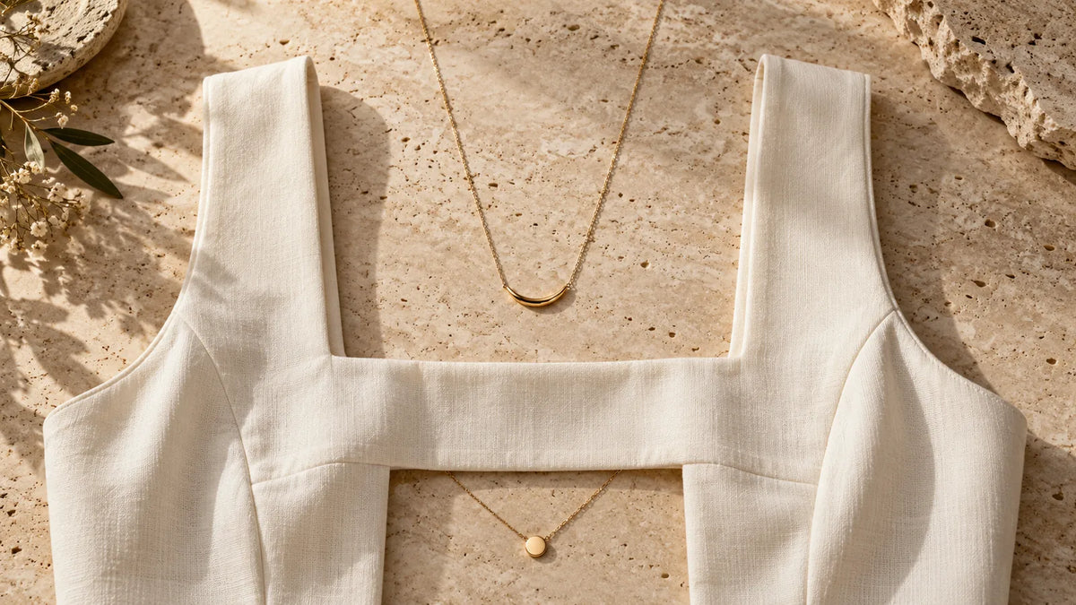 Ivory square-neck fabric with a fine gold-tone chain above its neckline and a pendant chain below.